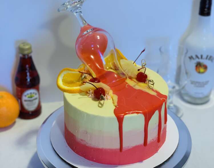 Malibu Sunset Cake - red, orange, and yellow ombre frosting, decorated with a pink drip and cocktail glass