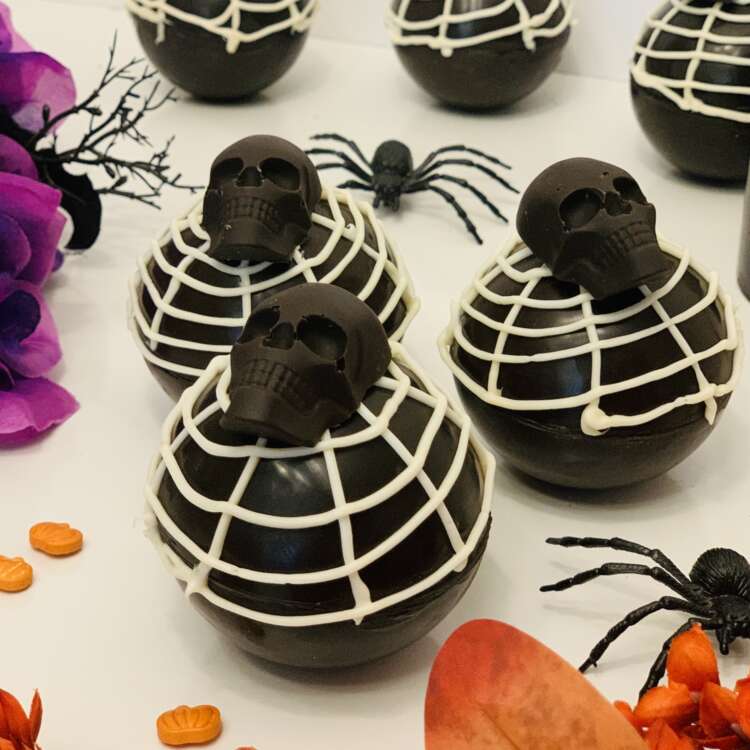 Halloween Hot Cocoa Bombs. Decorated with white candy melt spiderwebs and a black chocolate skull.