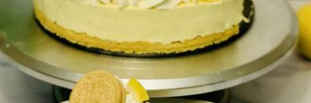 Lemon Oreo Cheesecake (no-bake) thumbnail image - slice cut from cheesecake in foreground, yellow lemon cheesecake decorated with lemon spirals, lemon Oreos, and whipped cream in the background